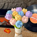 Colorful knitted flower bouquet in a white vase on a textured surface.