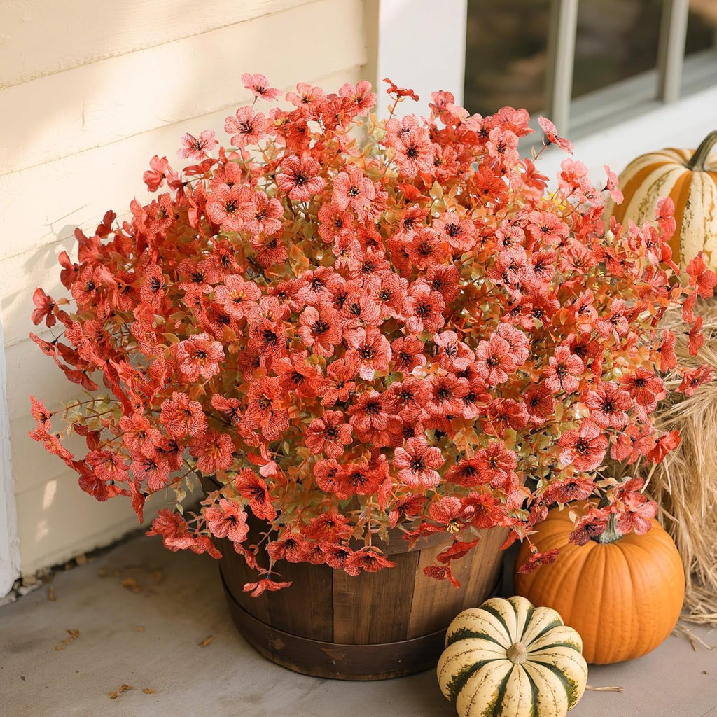 Bouquet of red flowers in a wooden basket with pumpkins and hay bale on a porch.