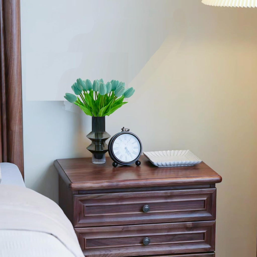 Wooden nightstand with decorative items including a vase of green tulips, clock, and square plate.