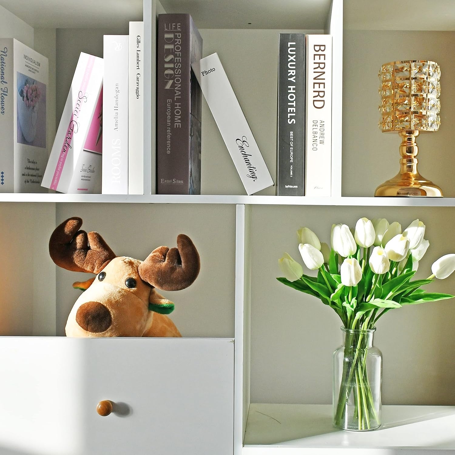 Bookshelf with books, a plush moose toy, and a vase of white tulips.