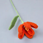 Crocheted orange flower with a green stem on a light gray background