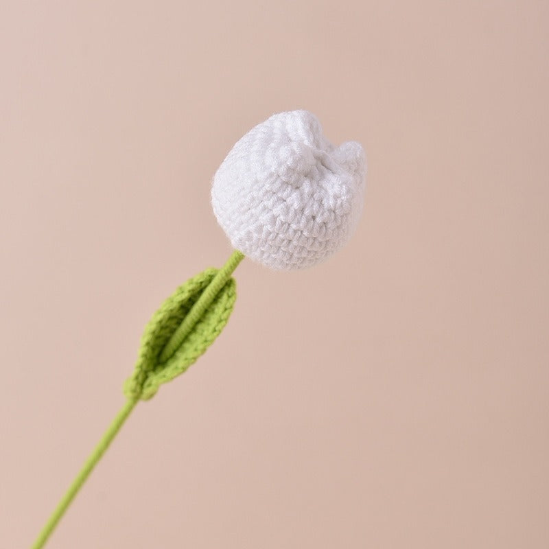 Knitted flower with white bloom and green stem on a beige background