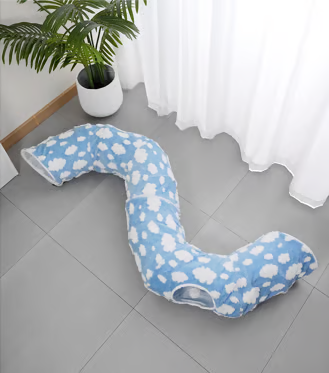 Blue and white cloud-patterned pillow on a gray floor with a plant and white curtain in the background.