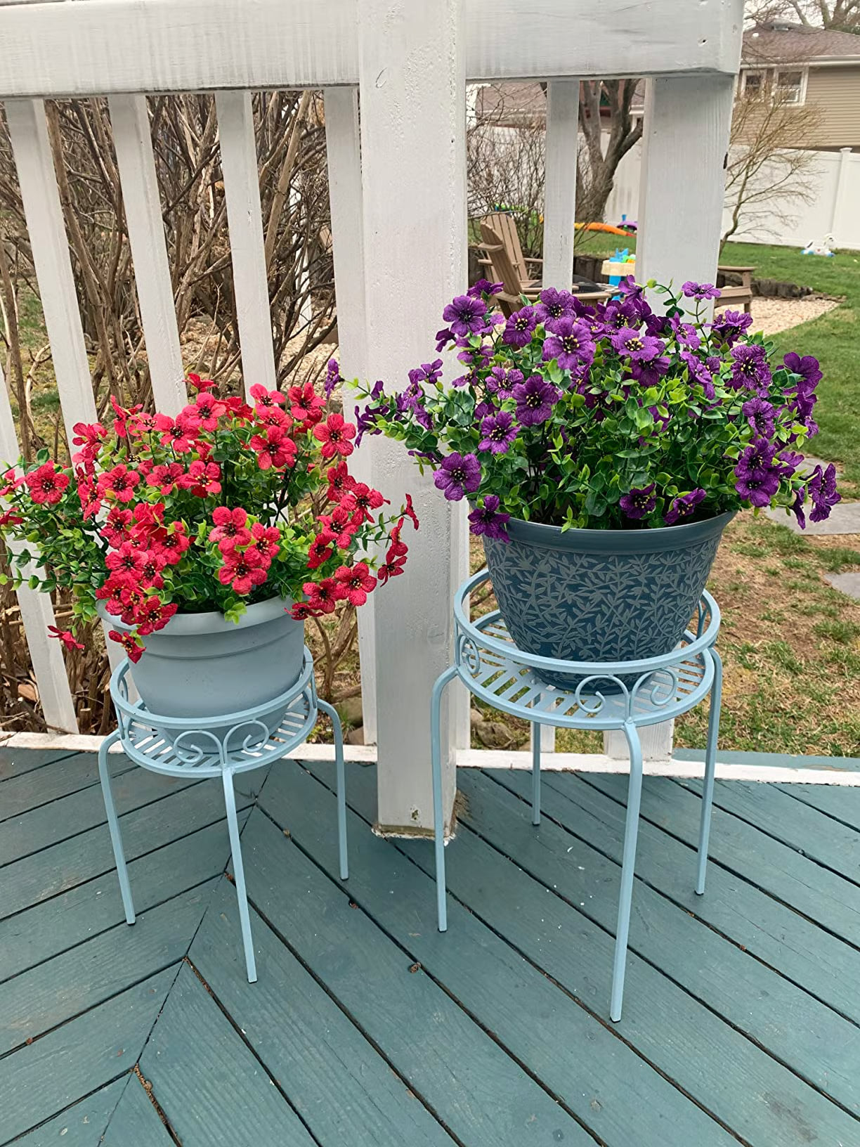 Two potted plants on small stands on a wooden deck with a white railing.