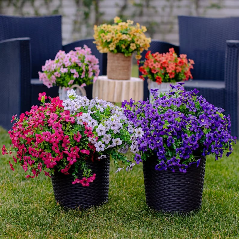 Colorful potted flowers on a grassy area with chairs in the background
